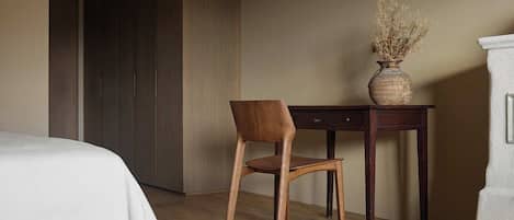 Un dormitorio con cama, una silla de madera, un escritorio y un jarrón con flores secas.