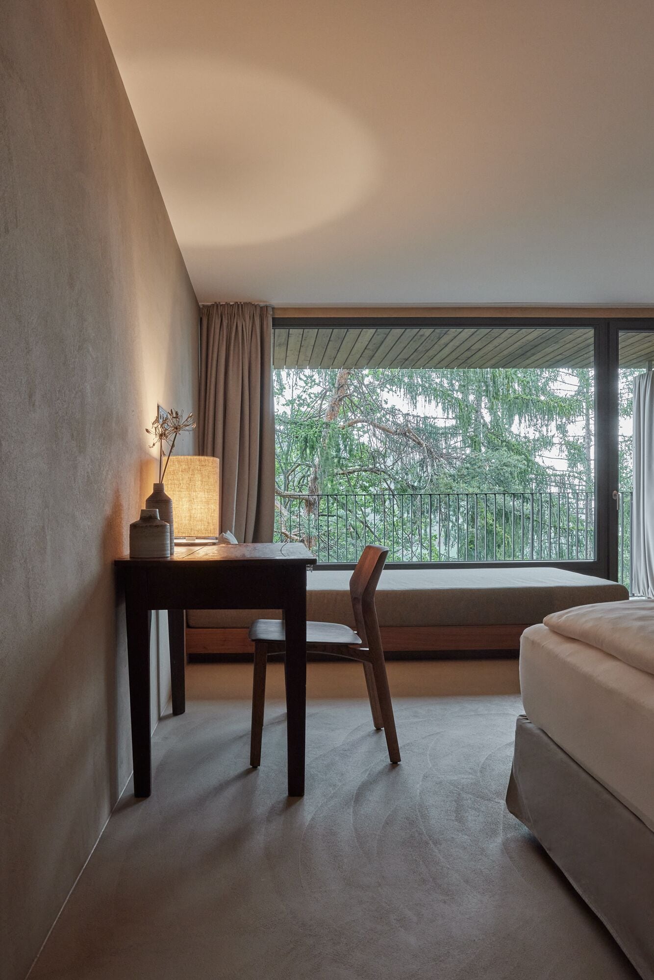 A modern hotel room with a large window, a desk, a chair, and a bed.