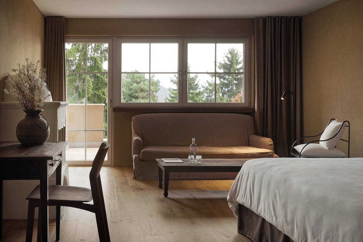 Une chambre d’hôtel comprenant un lit, un canapé, une table basse, un bureau avec une chaise et une fenêtre avec des rideaux.