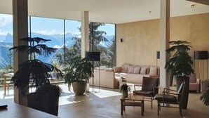 Una sala de estar moderna con un amplio ventanal que ofrece vistas a la montaña, un sofá, dos sillones y varias plantas en macetas.