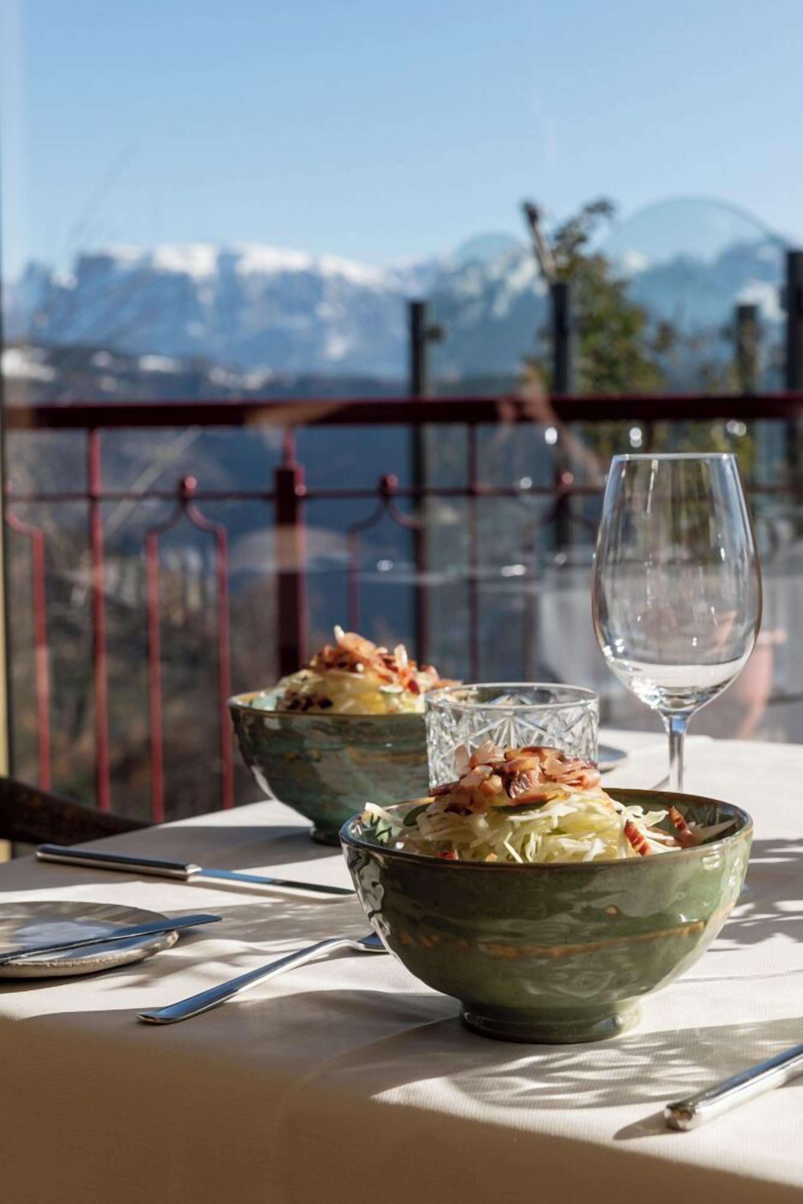 A table with two bowls of food and a wine glass, set against a scenic mountain backdrop.