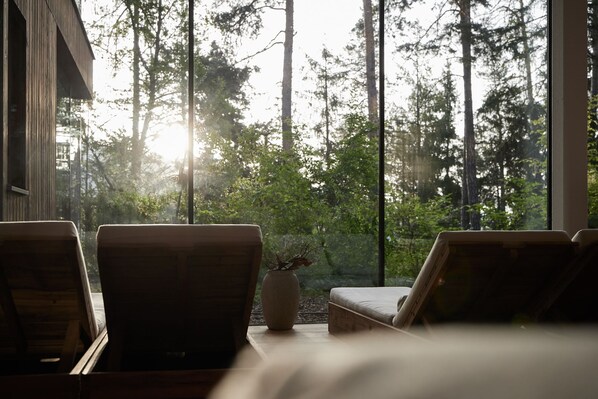 A room with a large window overlooking a forest, two wooden chairs, and a small table with a vase. - Hotel Saltus (San Genesio Atesino)