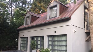 Una casa moderna de dos pisos con techo de tejas, ventanas grandes y un patio cubierto con mobiliario exterior.