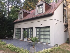 Una casa moderna de dos pisos con techo de tejas, ventanas grandes y un patio cubierto con mobiliario exterior.