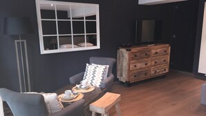 Un comedor con una mesa lista para dos personas, un sofá, un aparador de madera y un televisor en la pared.
