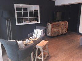 Un comedor con una mesa lista para dos personas, un sofá, un aparador de madera y un televisor en la pared.