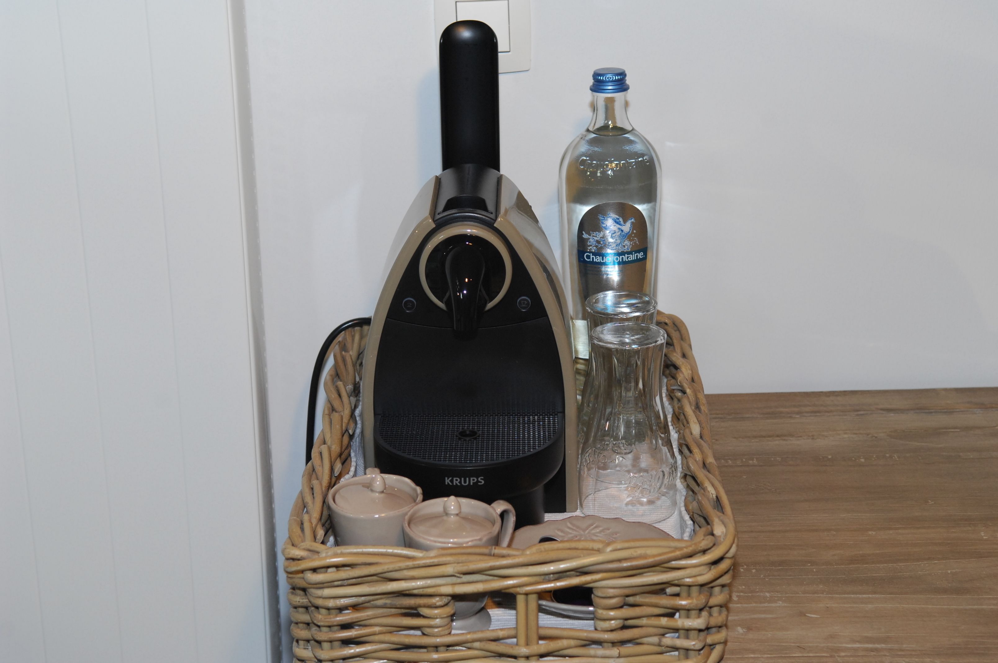 A wicker basket containing a vacuum cleaner, a bottle of Chouffontaine, two mugs, and a small container.