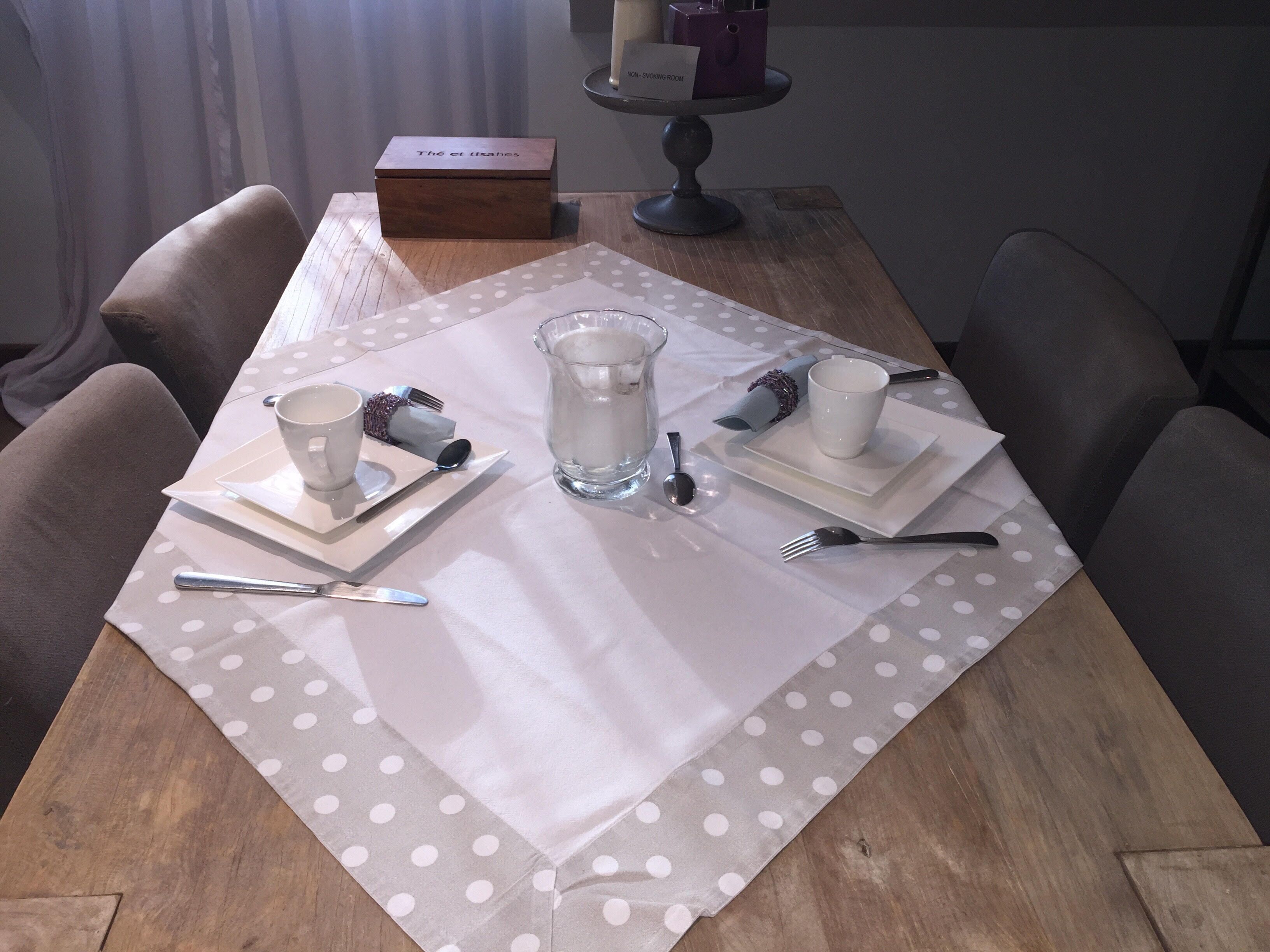 A dining table set with a white tablecloth, two white cups, a glass pitcher, cutlery, and a box labeled "The 6 et lissahes".
