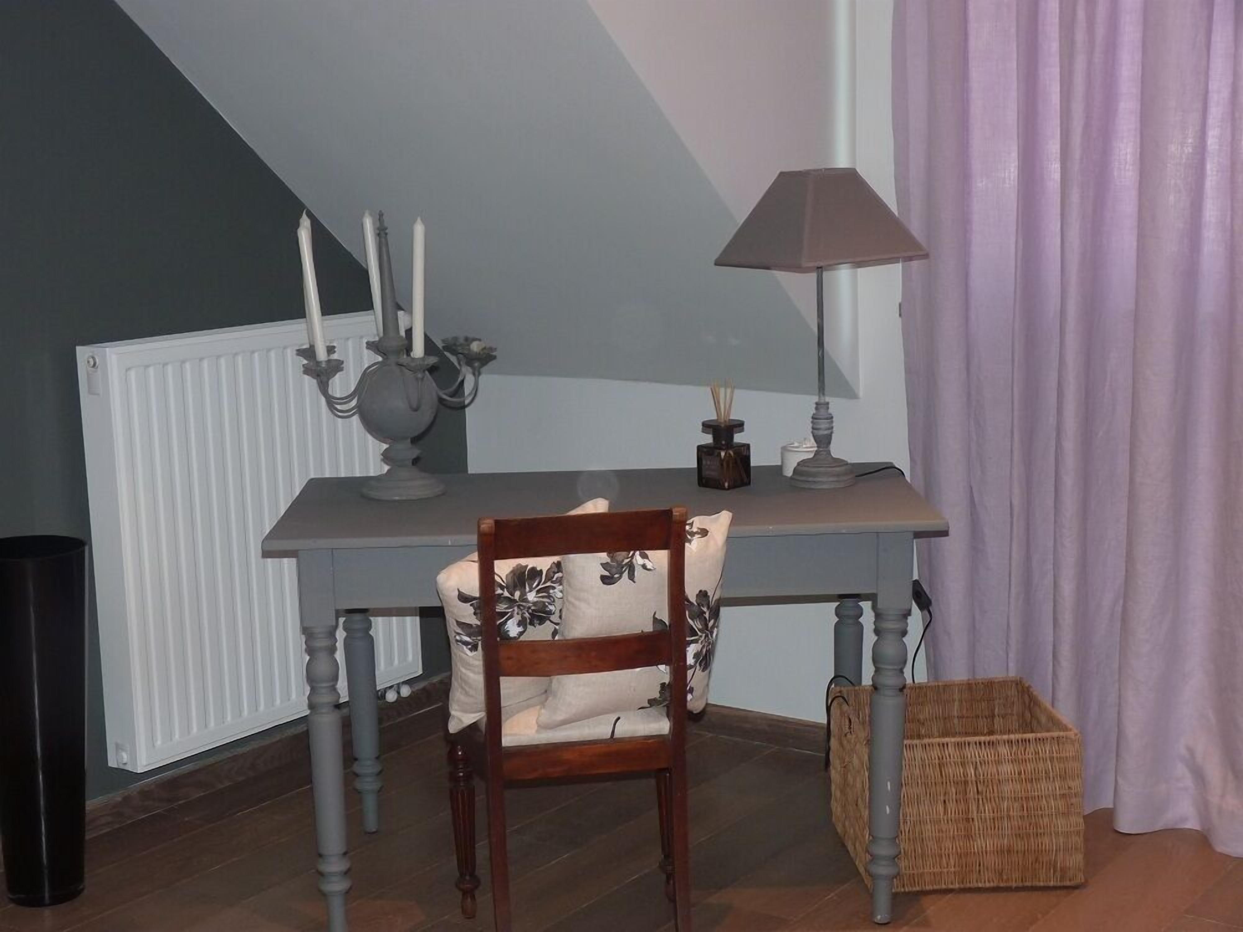 Una habitación con una silla de madera, una mesa con lámpara, un radiador y una cesta de mimbre.