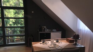 Un comedor con una mesa preparada para dos personas, una cocina al fondo y vistas a árboles a través de amplios ventanales.
