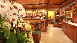 A bar area with a wooden bar counter, shelves with bottles, and a vase with flowers. - Albergo Ristorante Papa (Peschiera del Garda)