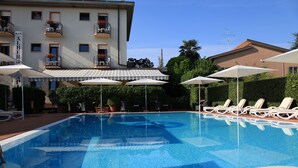 A swimming pool with lounge chairs and umbrellas, surrounded by a building with balconies and a clear sky. - Albergo Ristorante Papa (Peschiera del Garda)