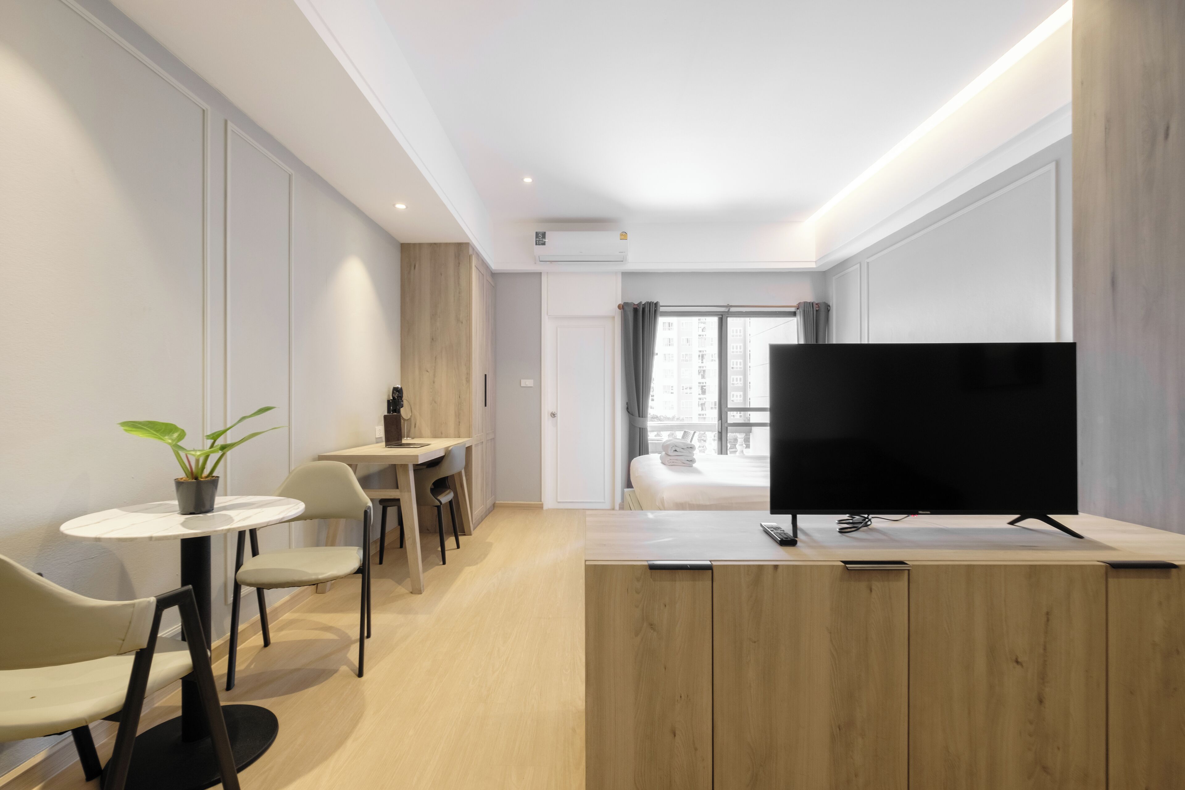 Een moderne hotelkamer met een houten kast, een flatscreen televisie, een klein rond tafeltje met stoelen, een kamerplant en een bed met uitzicht.
