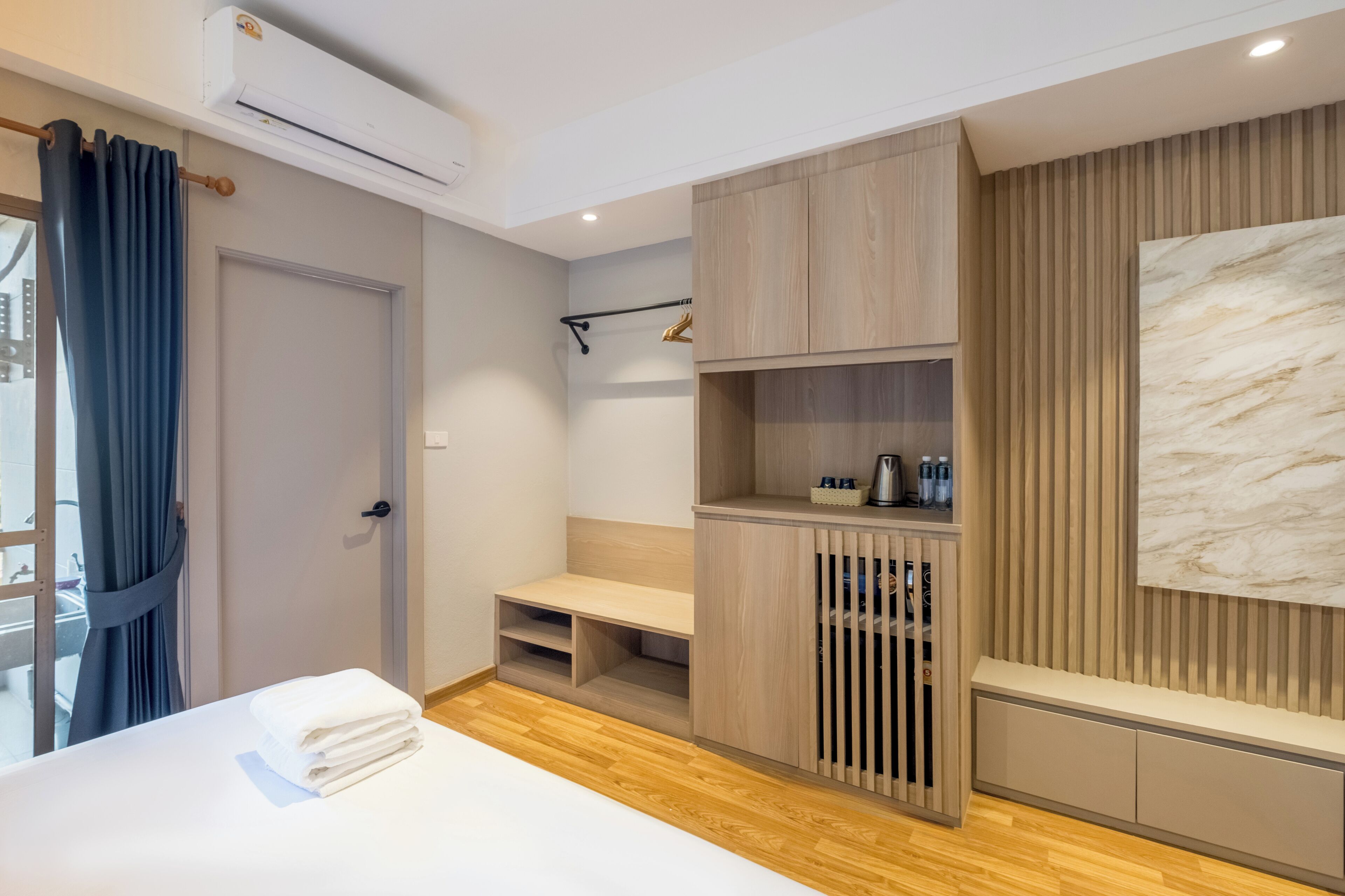 A modern hotel room with a bed, a bench, a wooden cabinet, and a marble wall.