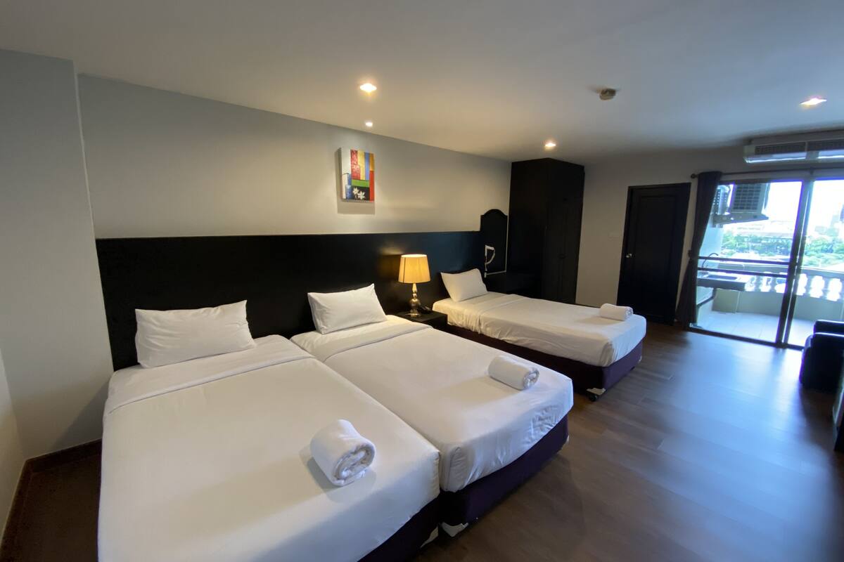Habitación de hotel con dos camas, un cuadro en la pared y un balcón con unidad de aire acondicionado.