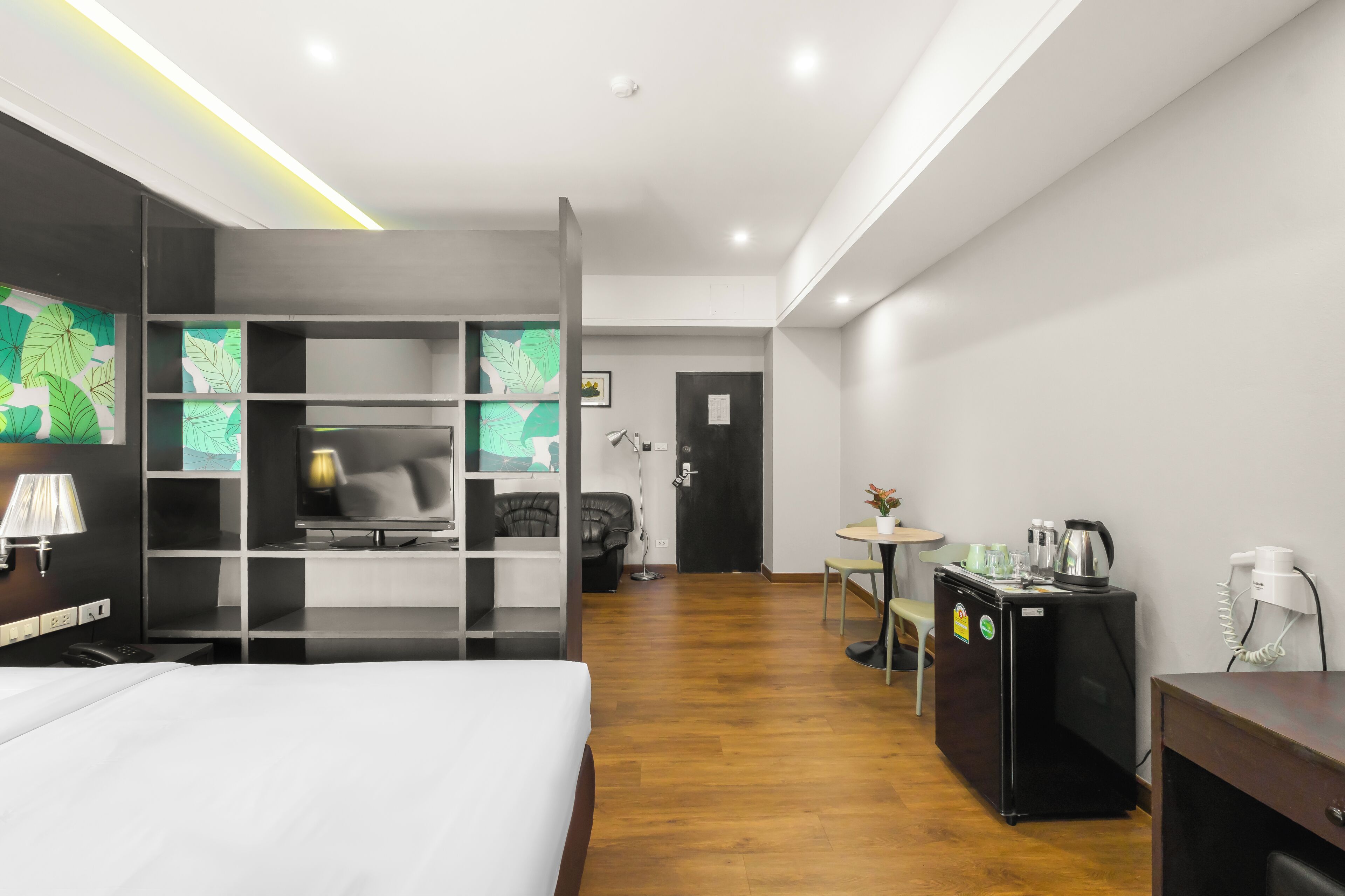 Een moderne hotelkamer met een bed, een bureau, een zwarte koelkast, een kleine tafel met een stoel en een kaart aan de muur.