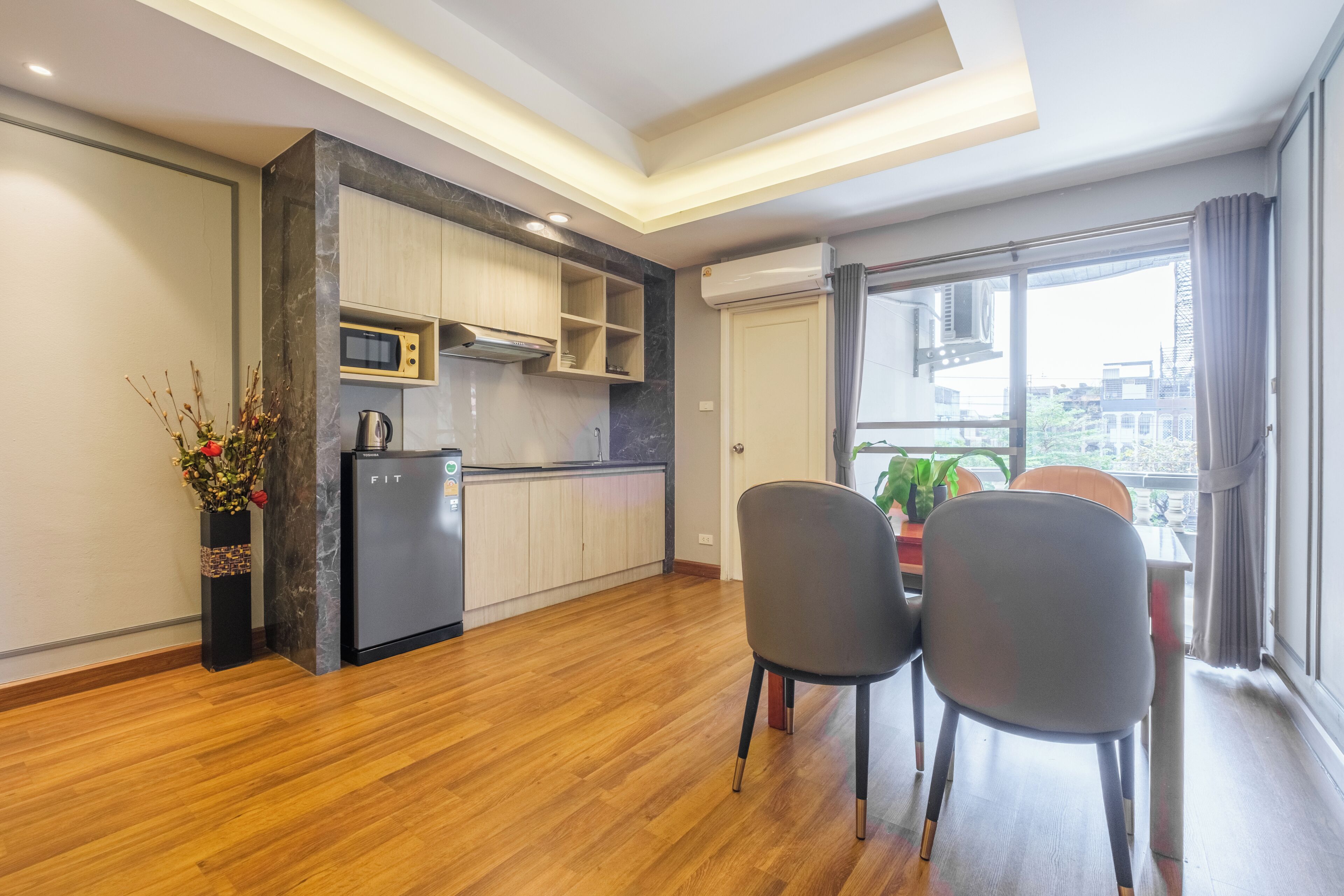 A modern kitchen with built-in appliances, a dining area with two chairs, and a large window offering a city view.