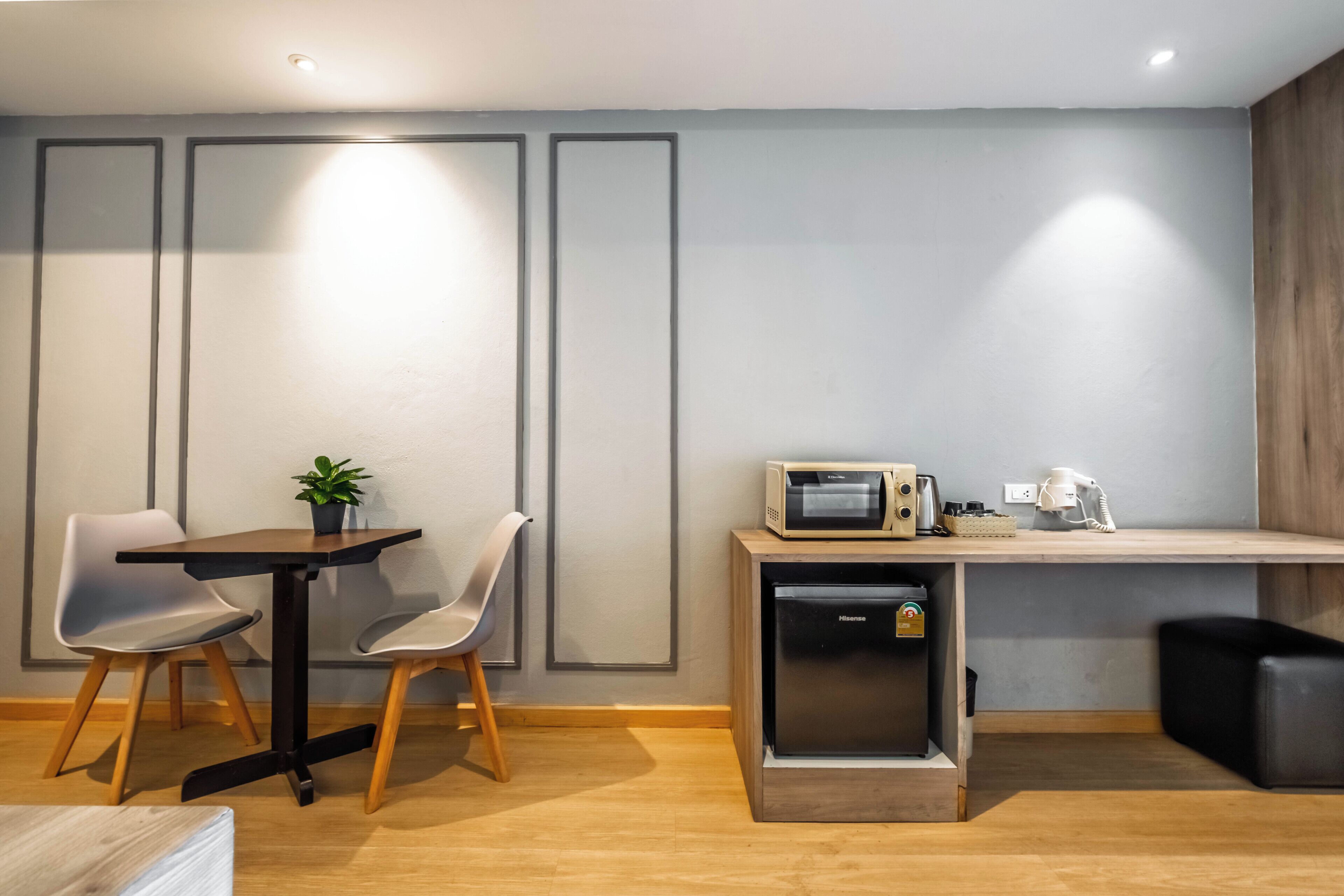Een moderne kitchenette met een magnetron, koffiezetapparaat en koelkast. Twee stoelen en een kleine tafel met een plantje.