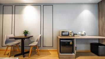 Een moderne kitchenette met een magnetron, koffiezetapparaat en koelkast. Twee stoelen en een kleine tafel met een plantje.