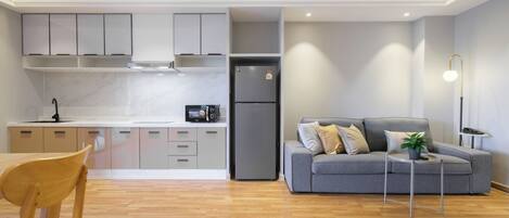 Een moderne keuken met grijze kastjes, een grijze koelkast en een eethoek met een houten tafel en stoelen.