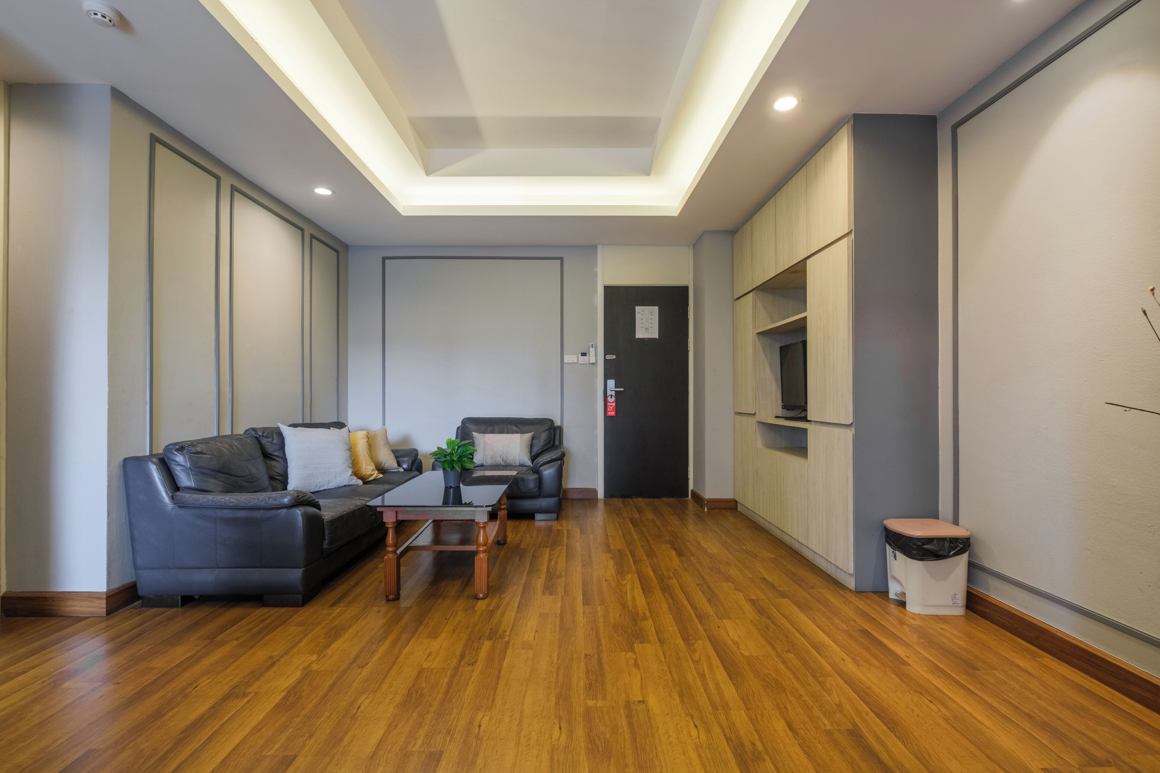 A modern living room with a wooden floor, a sofa, two armchairs, a coffee table, and a TV on a wooden cabinet.