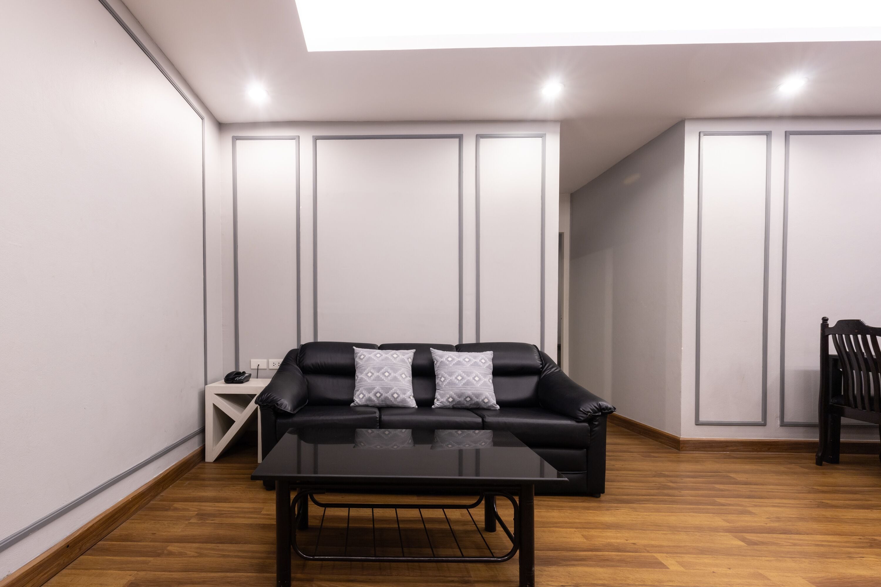 Un salon moderne avec un canapé en cuir noir, une table basse en verre et un plancher en bois.