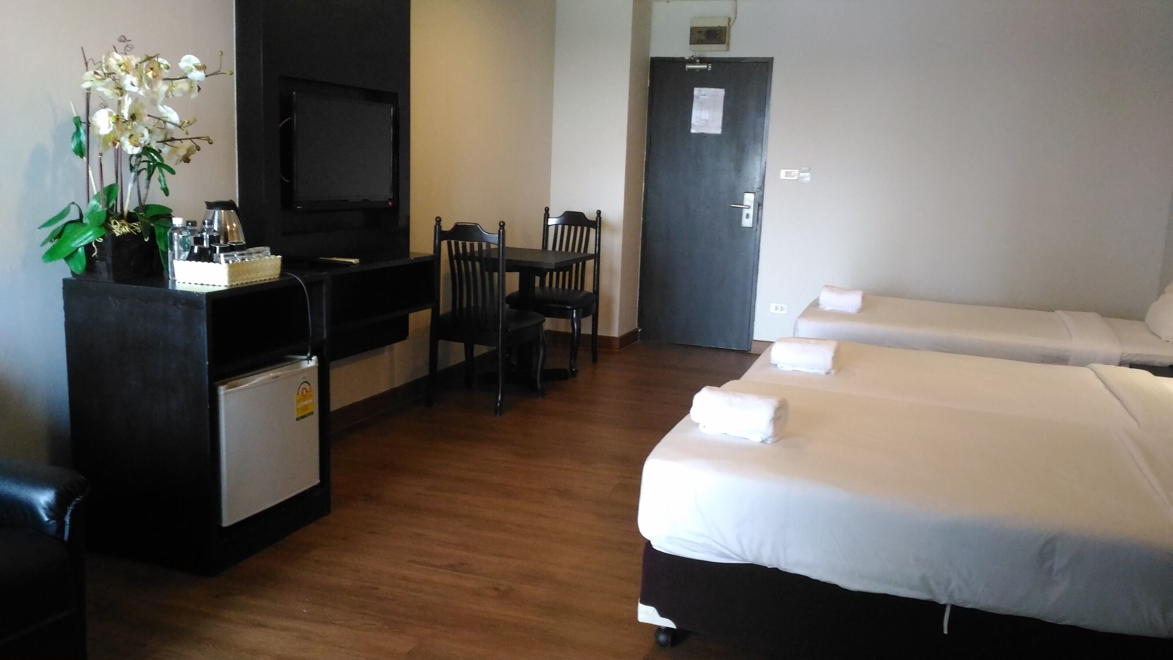 A hotel room with a wooden floor, a desk with a TV, a chair, and two beds with towels.
