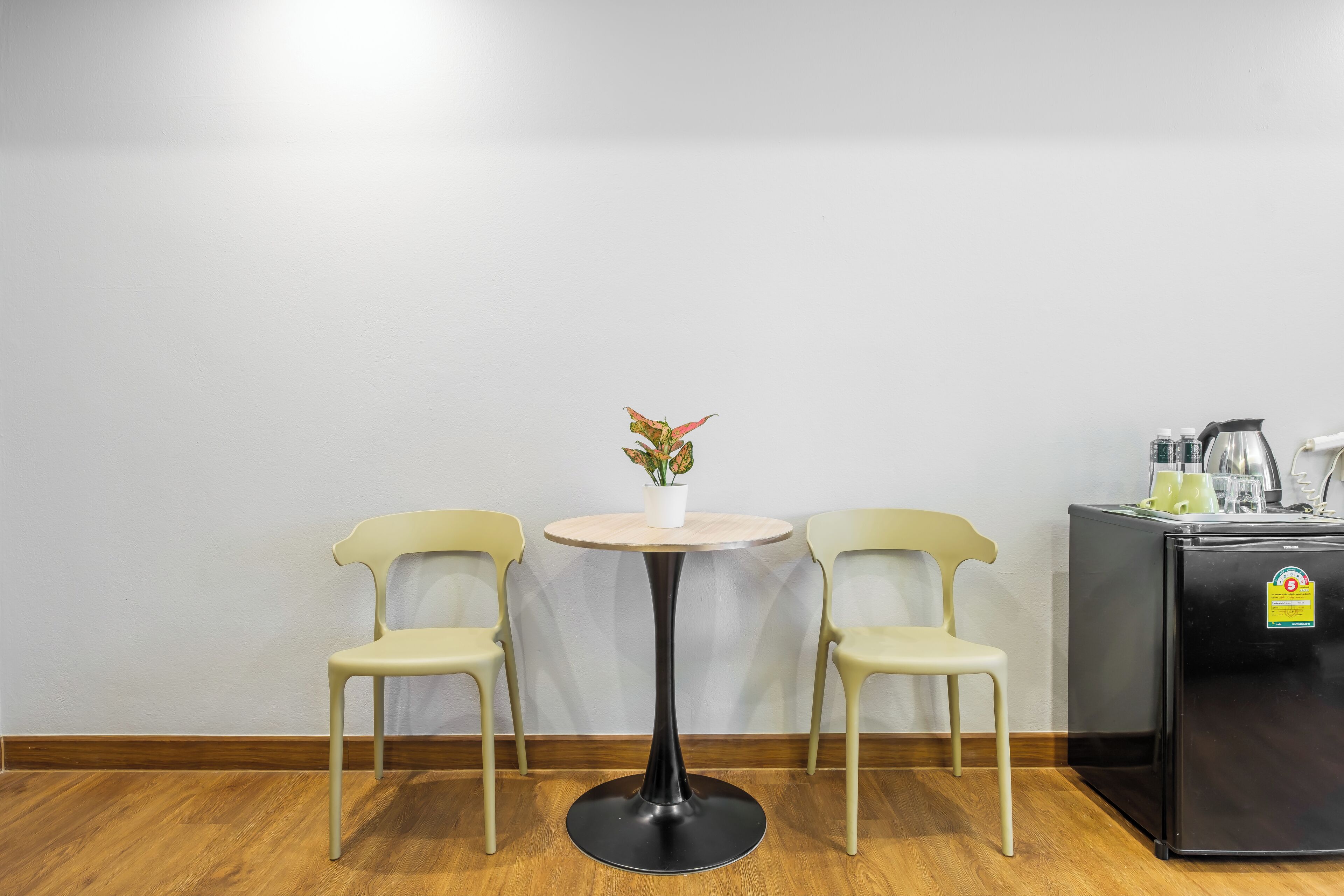 A small room with a round table, two chairs, a refrigerator, and a potted plant.