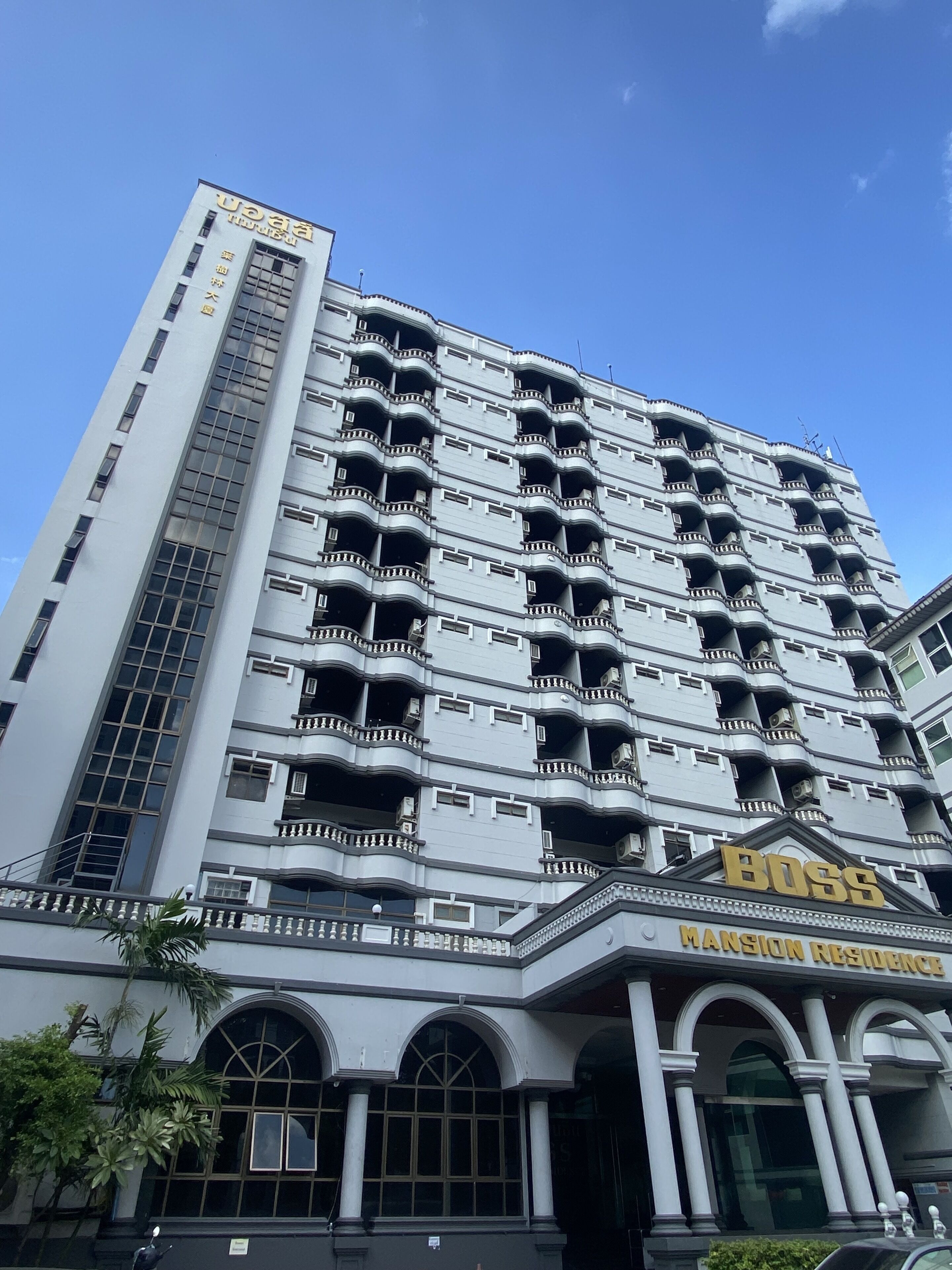 Un hôtel à plusieurs étages, dont le rez-de-chaussée est orné d’une grande enseigne « BOSS », indiquant la présence d’une section appelée « Résidence de luxe ».