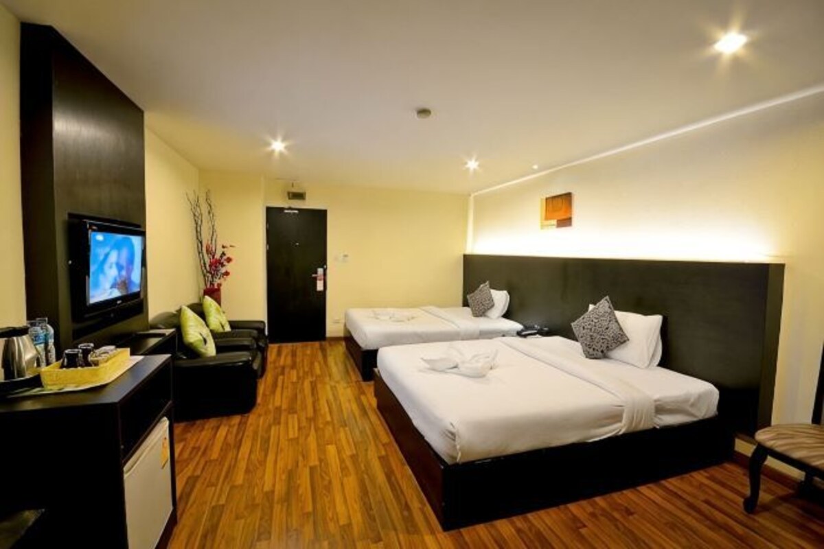 A hotel room with two beds, a desk with a TV, and a wooden floor.