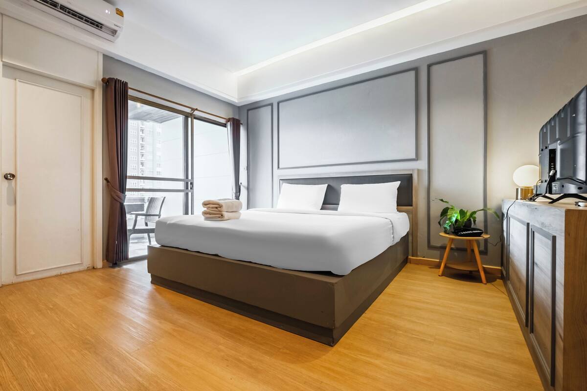 Una habitación de hotel moderna con una cama grande, un escritorio pequeño, un televisor y una ventana con cortinas.