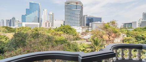 A cityscape with modern high-rise buildings, a balcony with a balustrade, and lush greenery in the foreground.