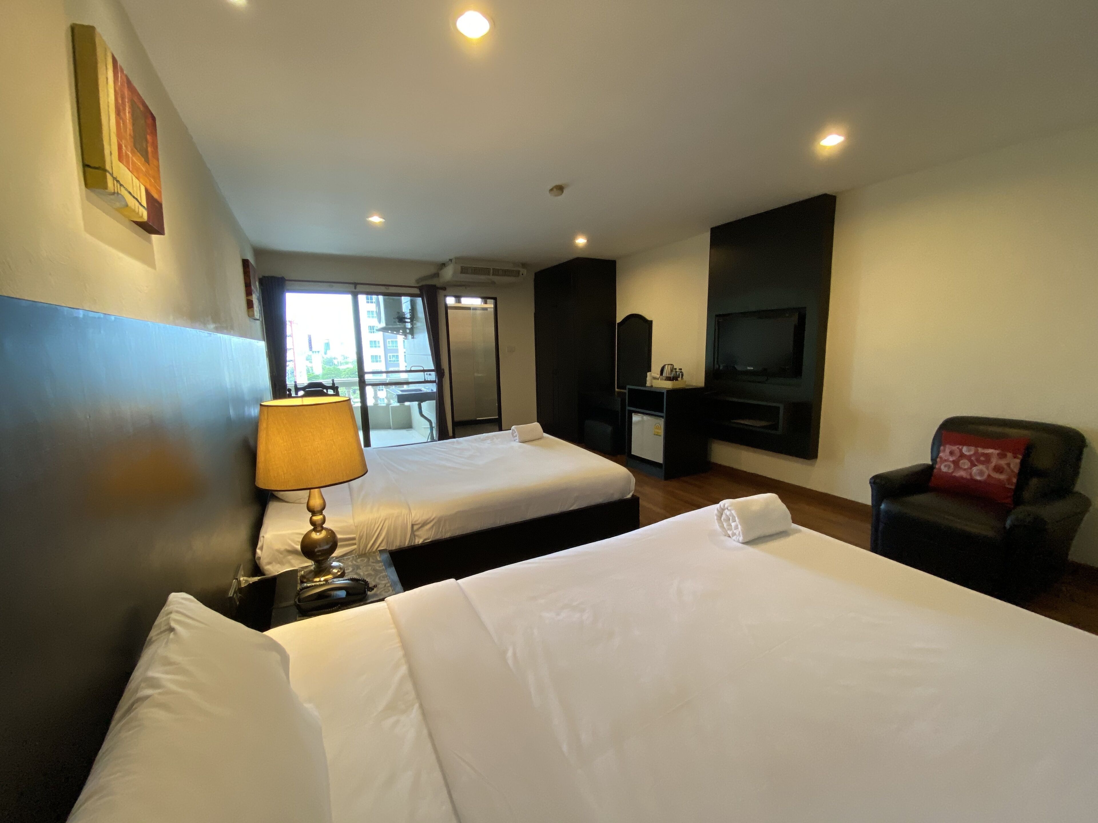 A hotel room with two beds, a desk, a chair, a TV, and a window with a view of buildings.