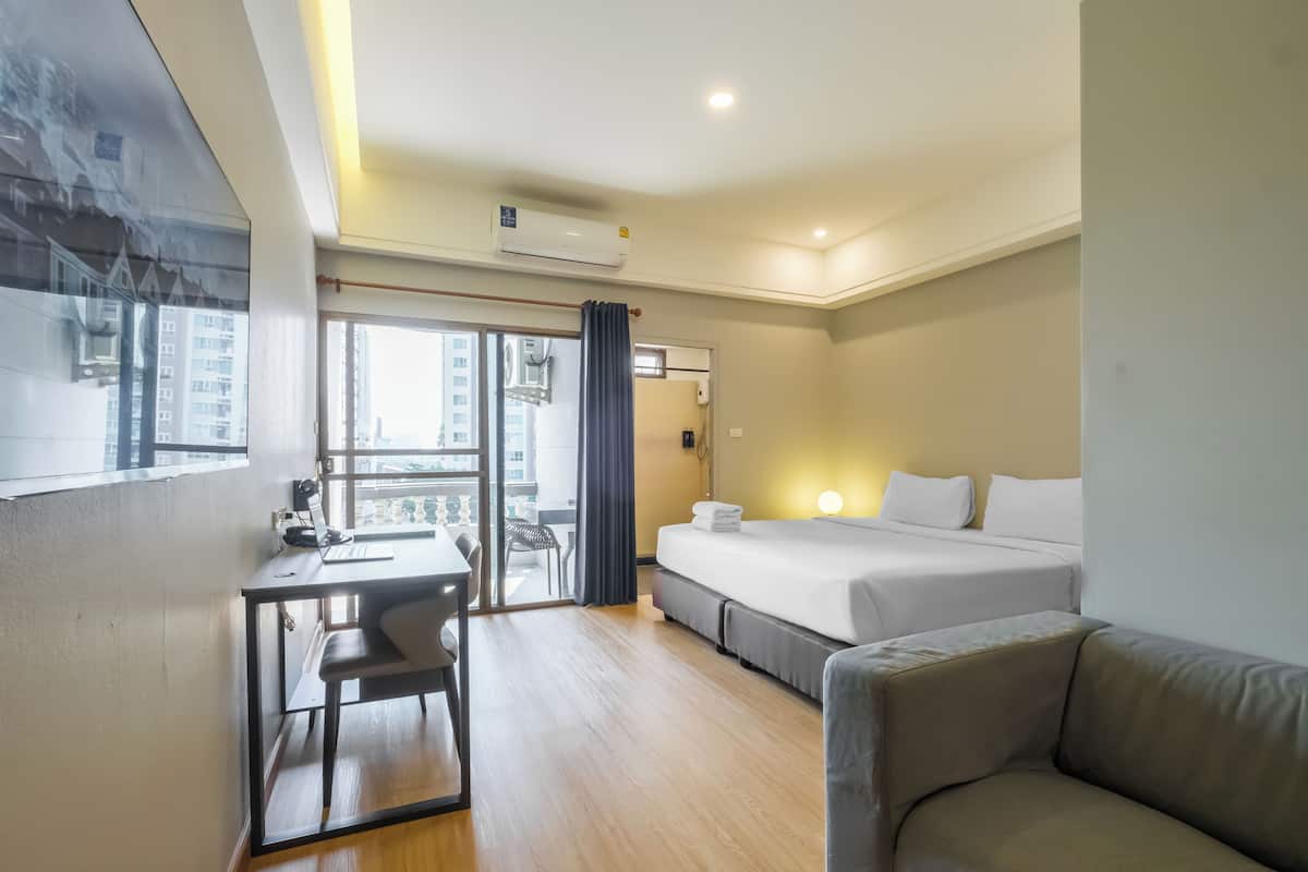 Habitación de hotel con escritorio, dos camas, un sofá y un balcón con vistas a edificios.