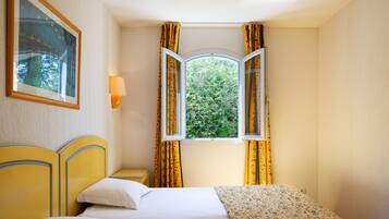 A hotel room with a bed, a nightstand, a lamp, and a window with curtains.