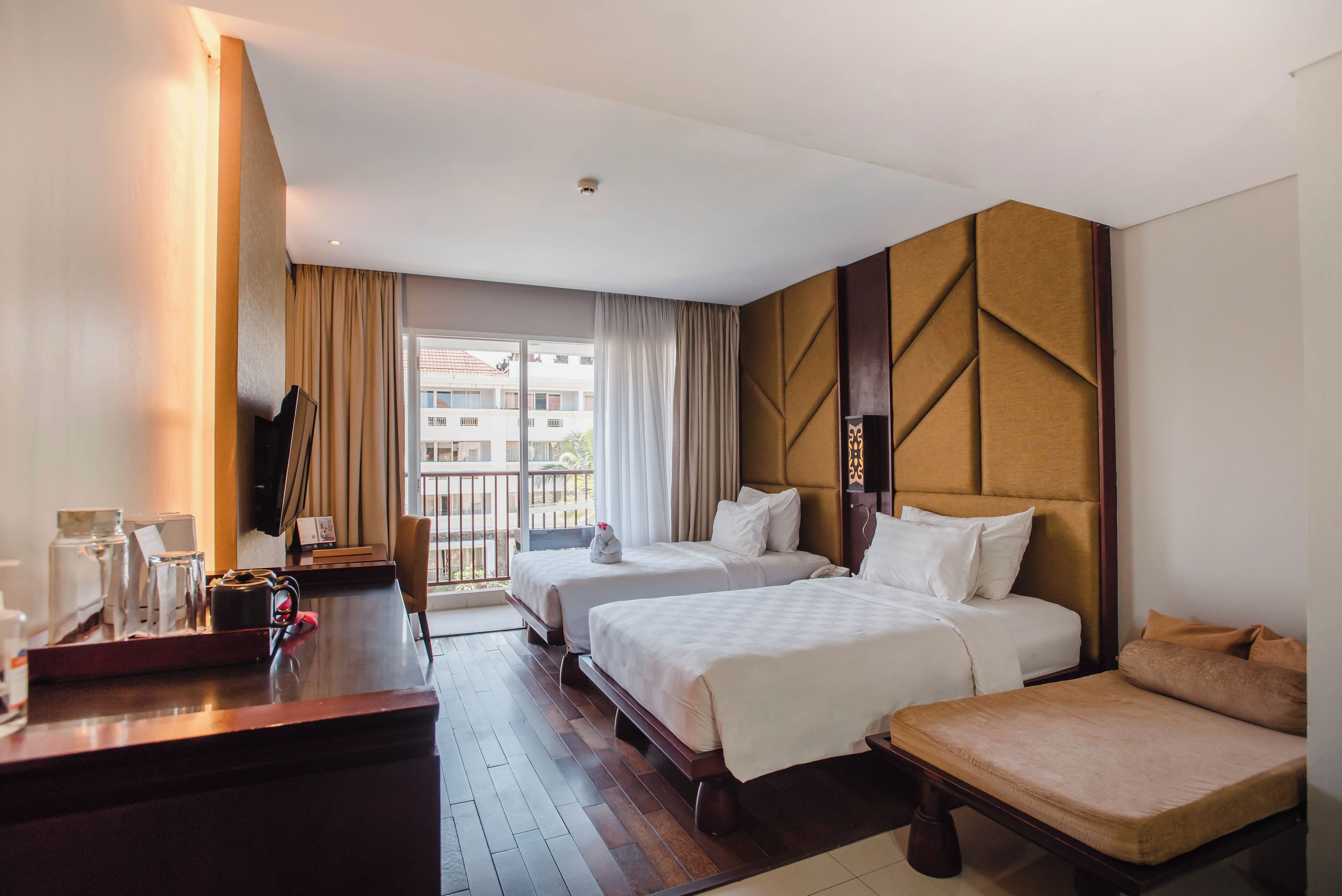 Habitación de hotel con dos camas, un escritorio y cafetera, y vista a un edificio desde la ventana.