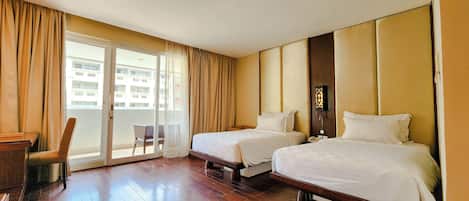 A hotel room with two beds, a chair, a desk, and a balcony with curtains.