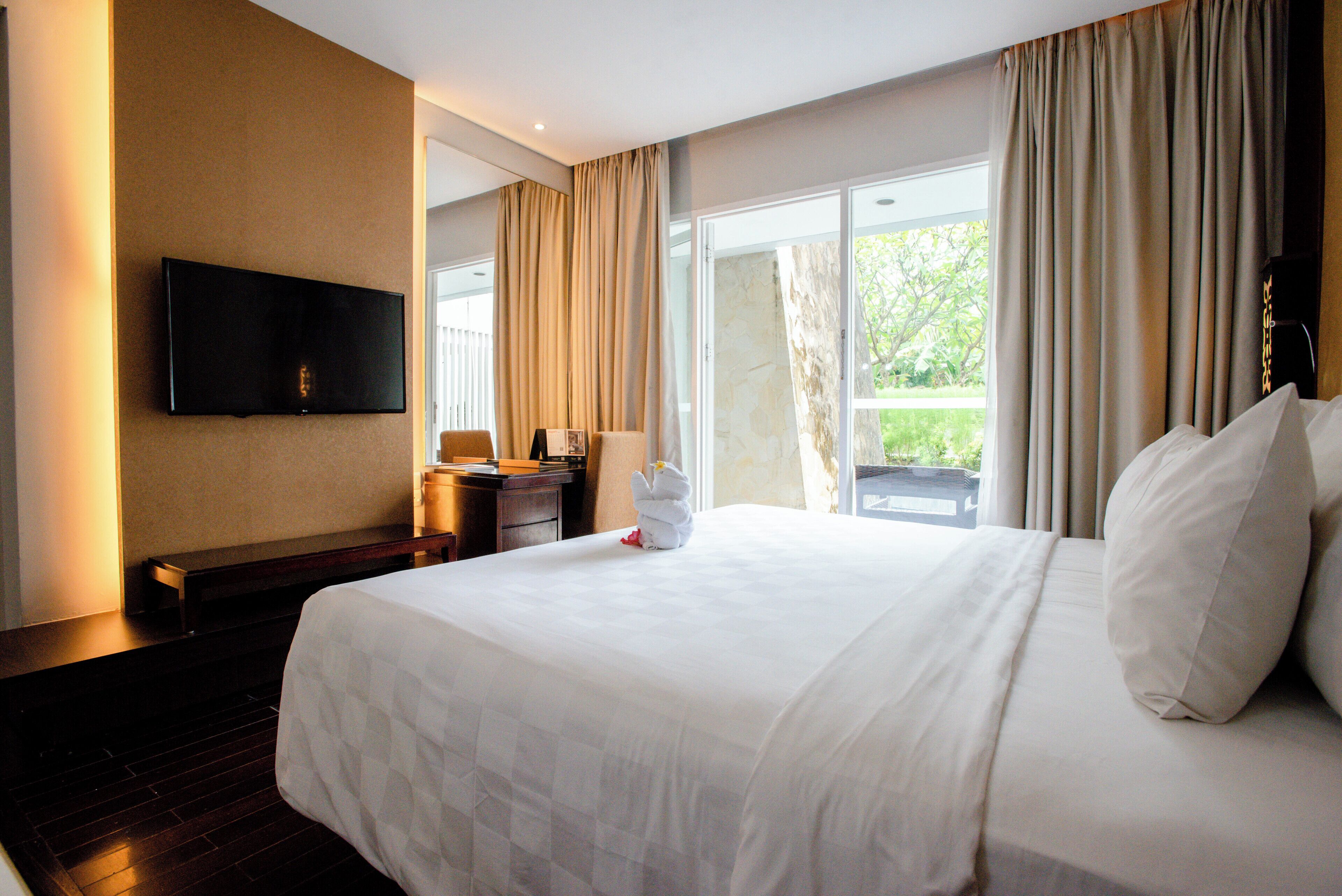 Habitación de hotel con una cama grande, un televisor de pantalla plana en la pared, un escritorio con silla y una ventana con cortinas.