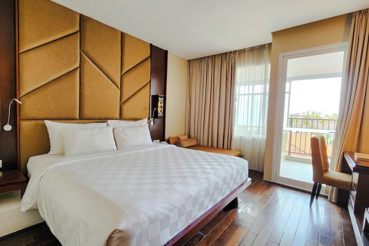 Een hotelkamer met een groot bed, een bureau, een stoel en een balkon met gordijnen.