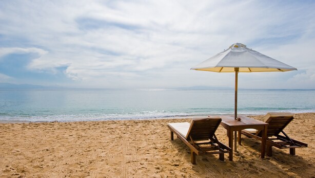 Une plage avec une chaise longue en bois, une petite table et un parasol.