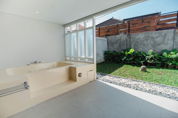 Une salle de bain moderne dotée d’une grande baignoire, d’une douche et offrant une vue sur un jardin avec des plantes et une clôture en bois.