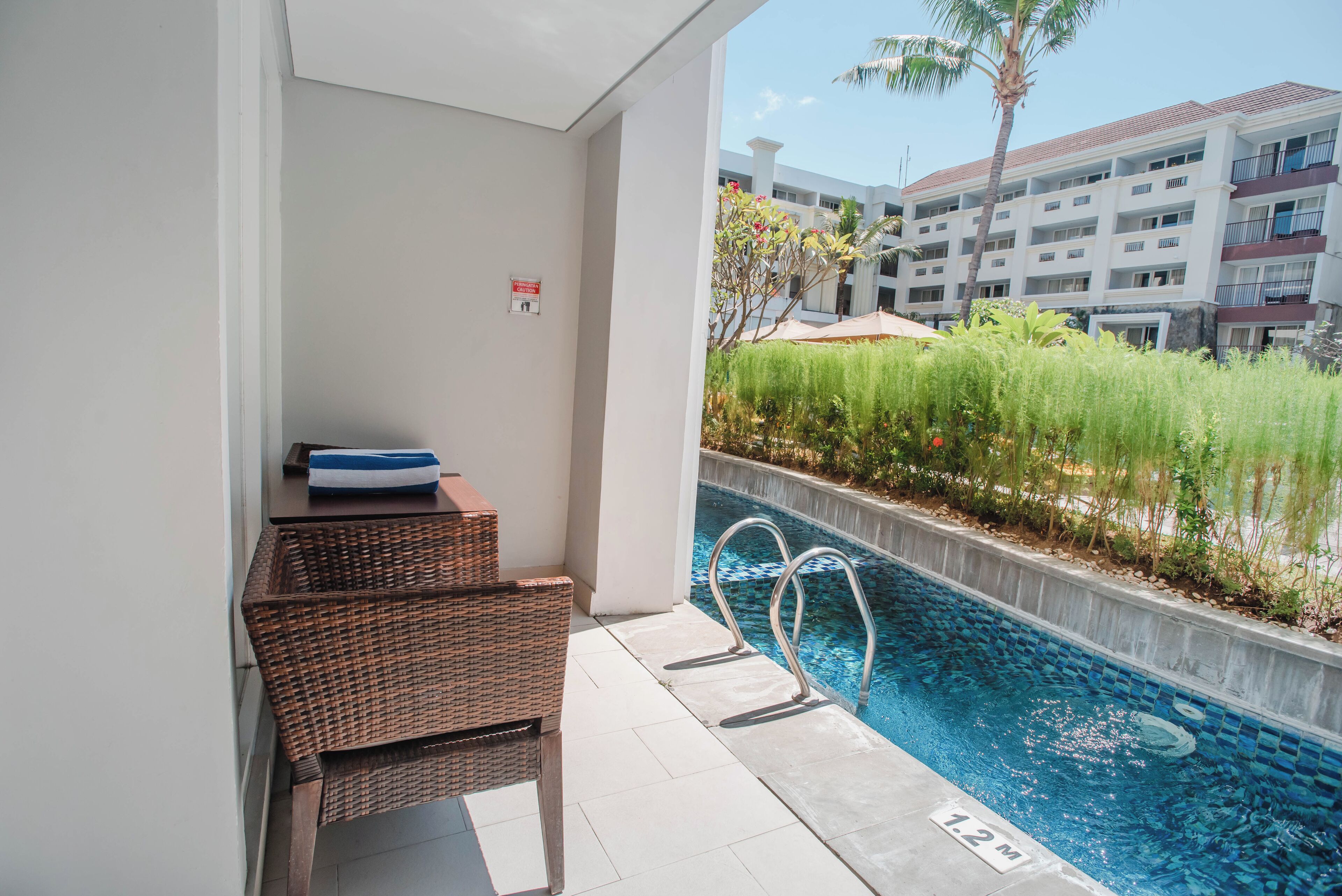 Un área junto a la piscina con mobiliario de mimbre, una piscina cristalina y una vista de un edificio de varios pisos al fondo.