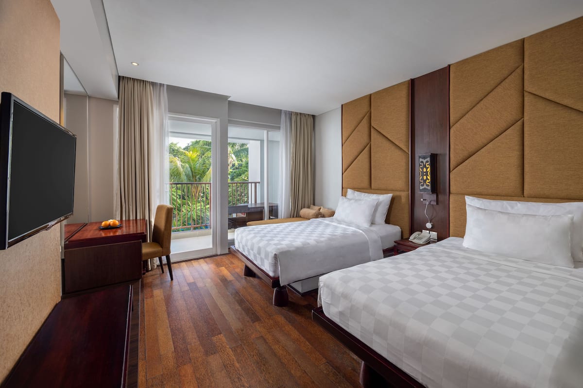 Een hotelkamer met twee bedden, een bureau, een stoel, een televisie en een balkon met gordijnen.