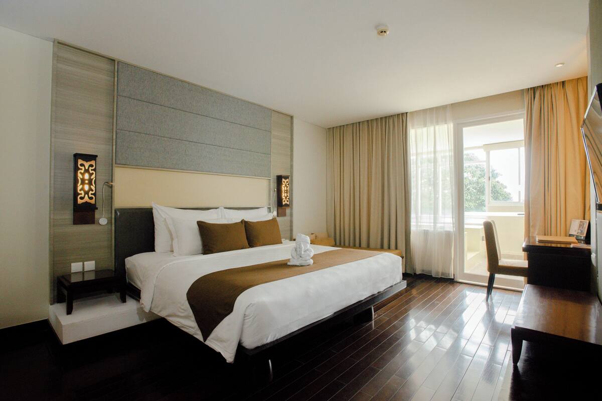 Hotelkamer met een groot bed, een bureau en een stoel. Er is een raam met gordijnen en uitzicht op buiten.