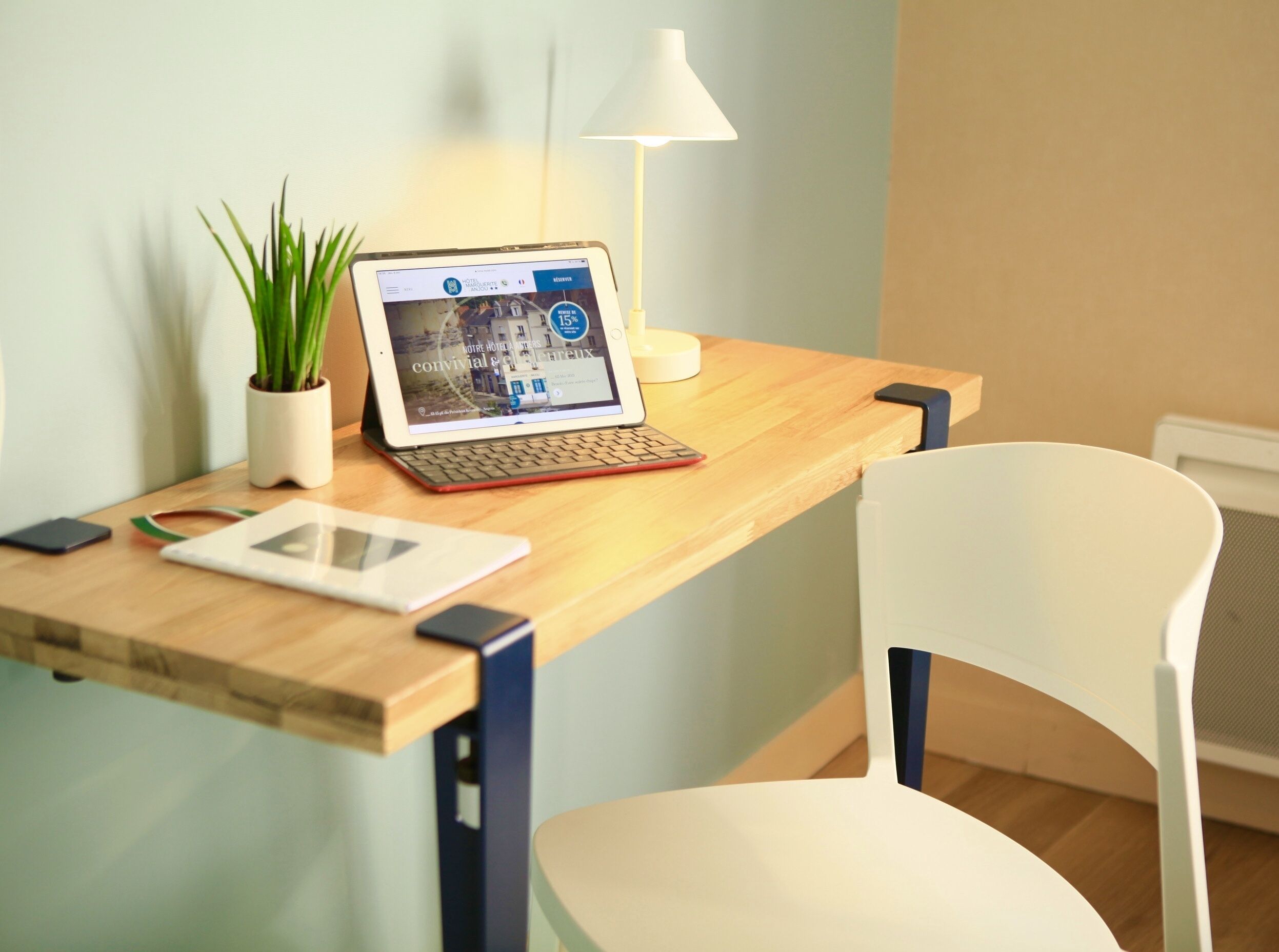 A laptop on a wooden desk with a tablet, a smartphone, and a potted plant.