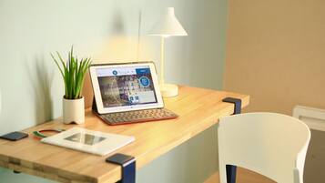A laptop on a wooden desk with a tablet, a smartphone, and a potted plant.