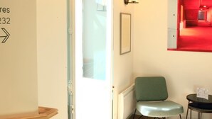 A room with a green chair, a small table, and a door leading to a red-lit area. - Marguerite d'Anjou (Angers)