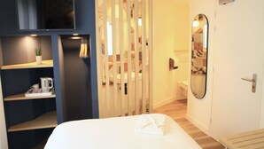A hotel room with a bed, a TV mounted on the wall, a shelf with a plant and a kettle, and a bathroom with a mirror and toilet. - Marguerite d'Anjou (Angers)