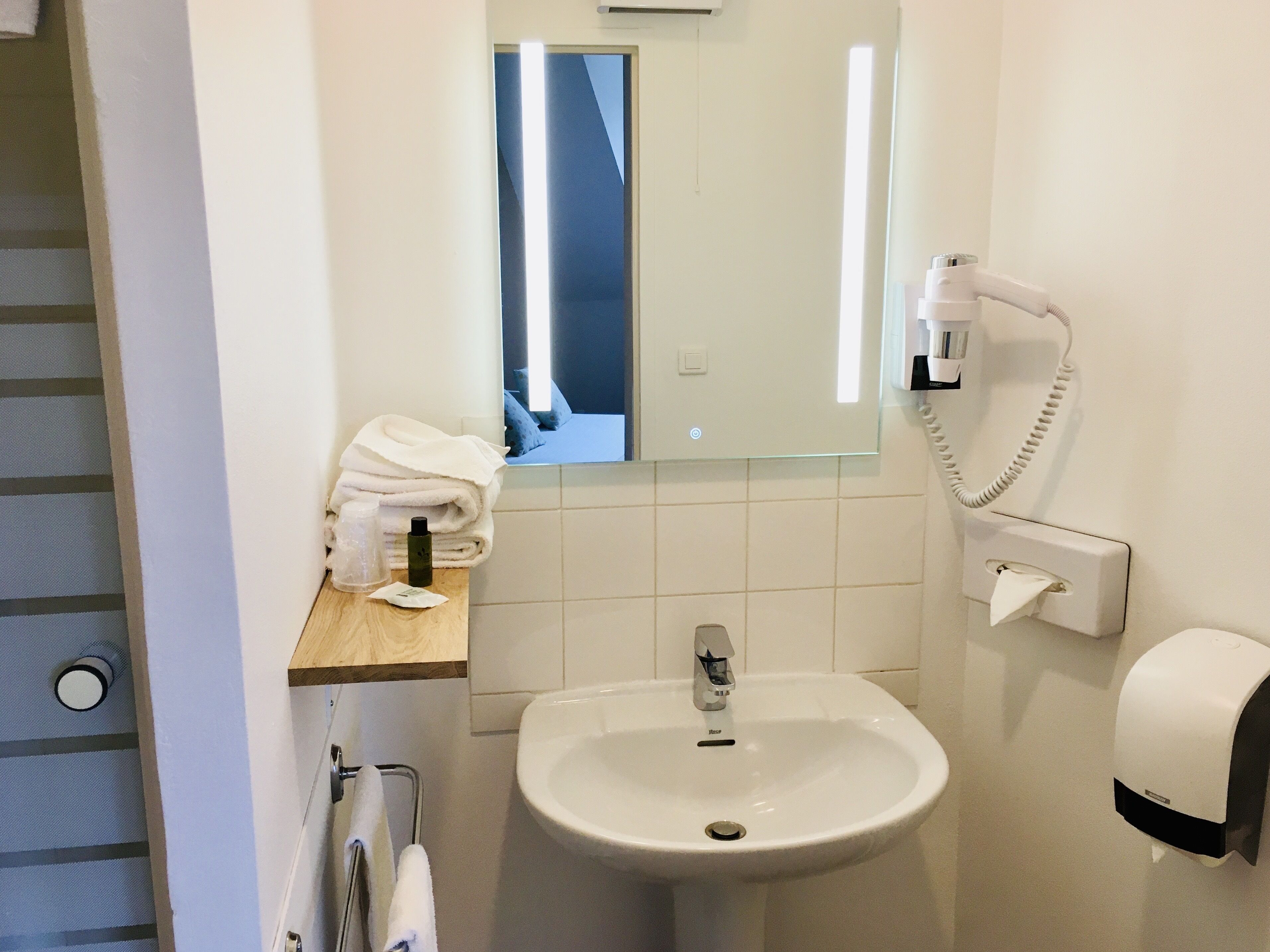 Un baño con lavamanos, espejo, toallero, secamanos y teléfono.