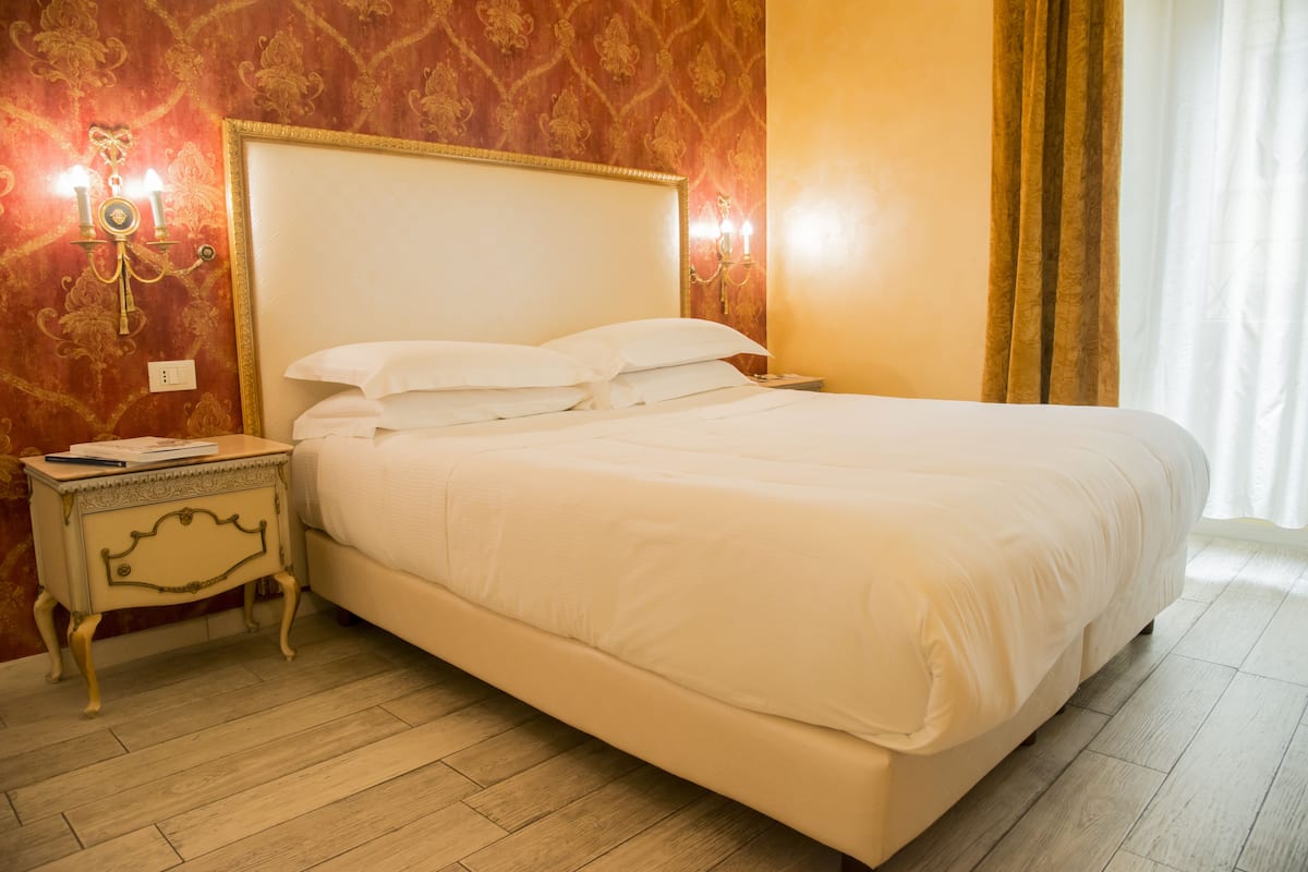 A neatly made bed in a room with patterned wallpaper and a wooden floor.